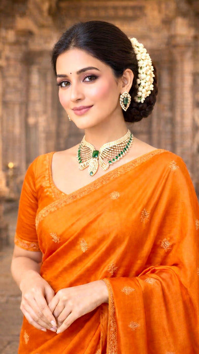 Woman in an orange saree with jewelry  and temple as a background