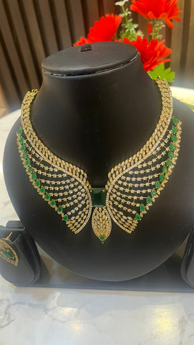 Gold and green necklace on a black mannequin bust with red flowers in the background