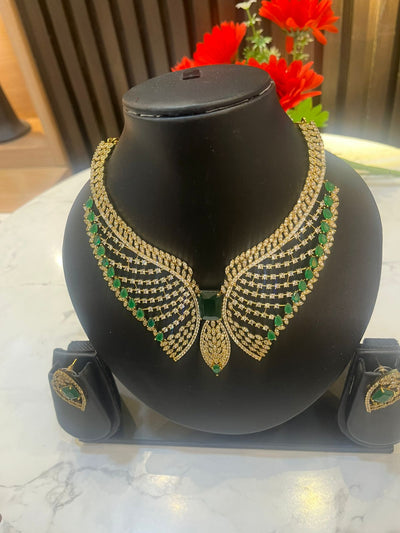 Gold and green necklace on a black mannequin bust with red flowers in the background