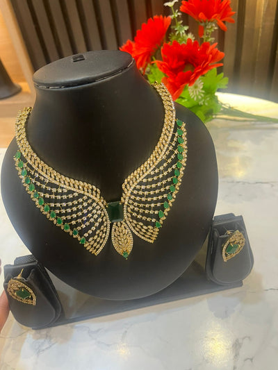Gold and green necklace on a black mannequin bust with red flowers in the background